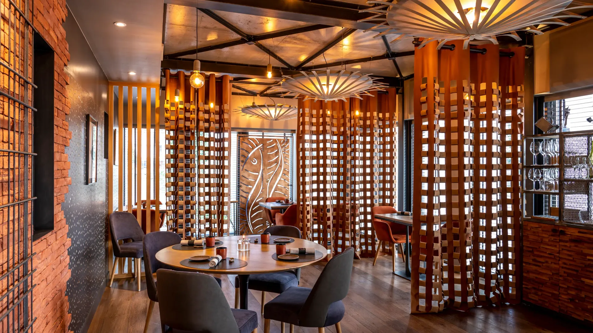 Restaurant intérieur avec des tables rondes, des chaises et des décorations en bois, éclairé par des lampes suspendues